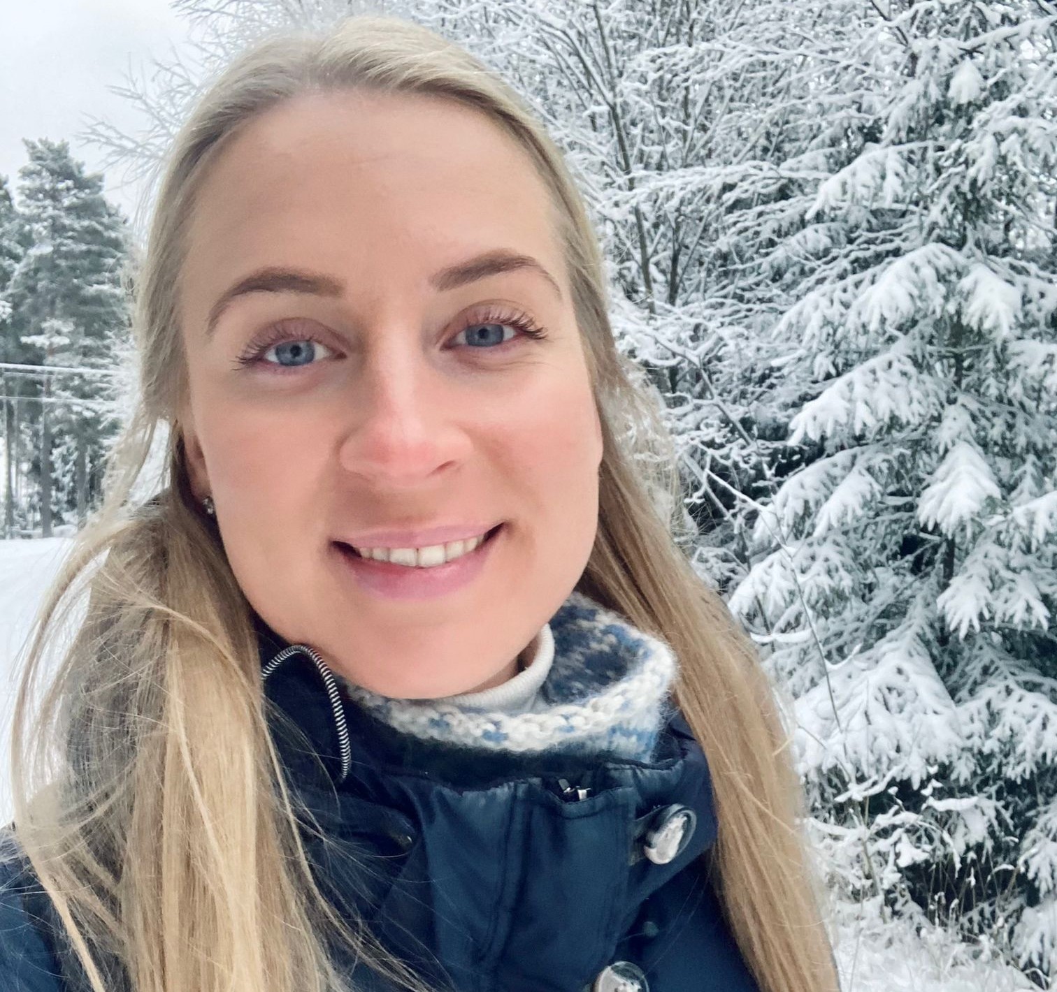 An image of a woman who's smiling at the camera. Outdoors, snow on the ground.