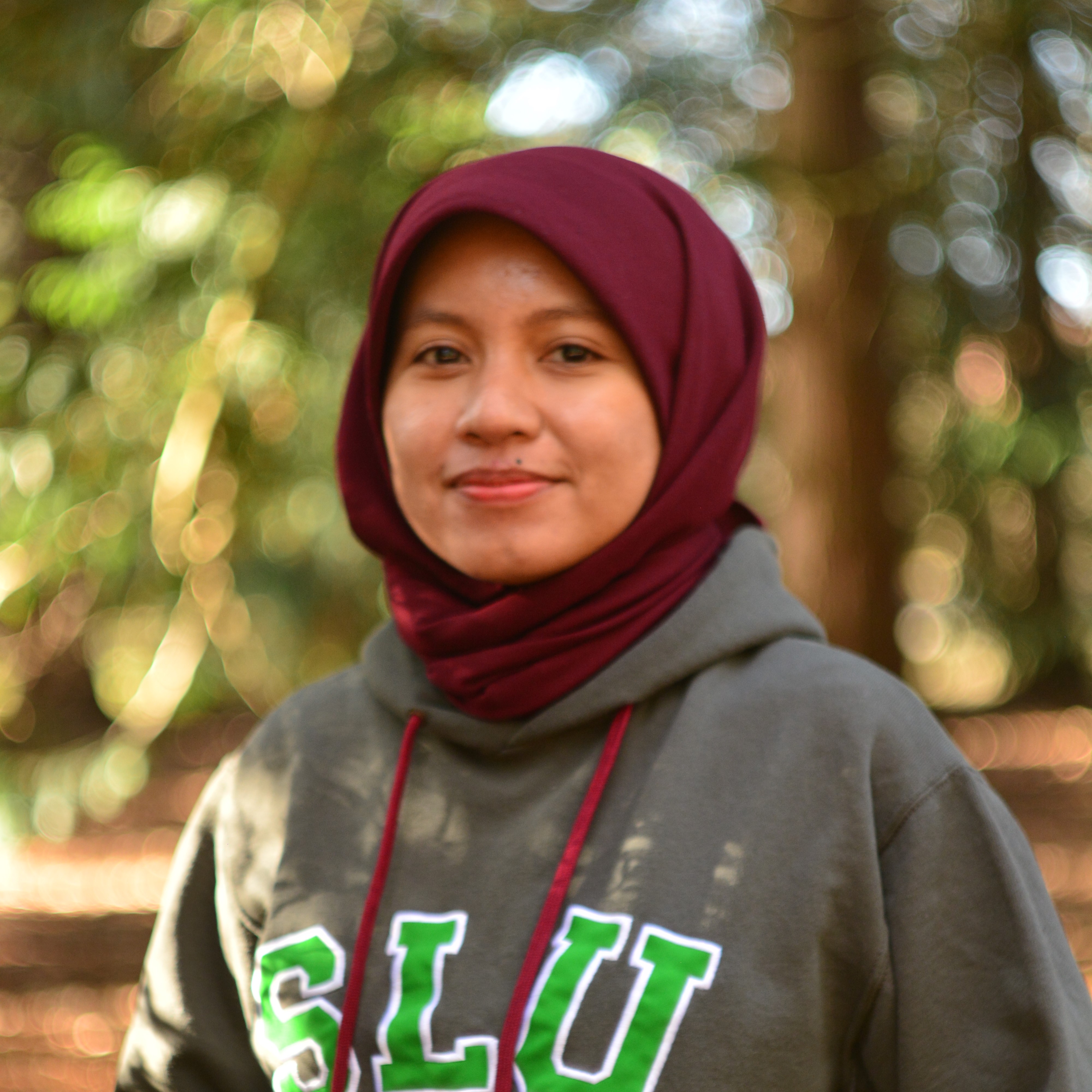 An image of a woman wearing a sweater with the text "SLU". Outdoors.