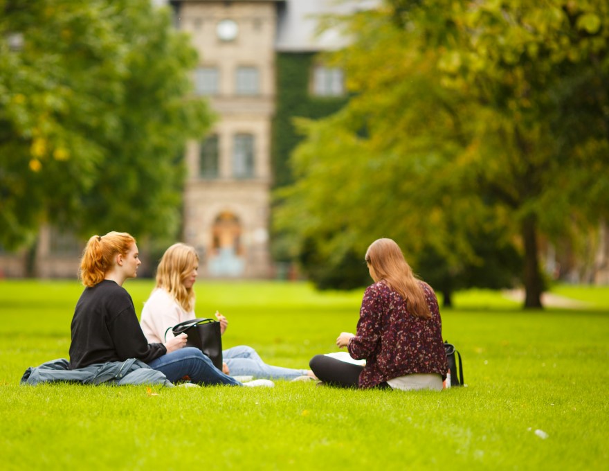 Tre studenter sitter på en gräsmatta. Foto