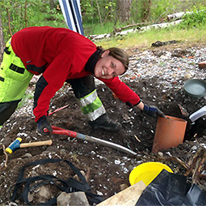 En kvinna i röd jacka gräver ett hål i marken, foto.
