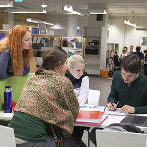 Four people are looking in a book togheter. Photo. SLU's library in Umeå. Photo.