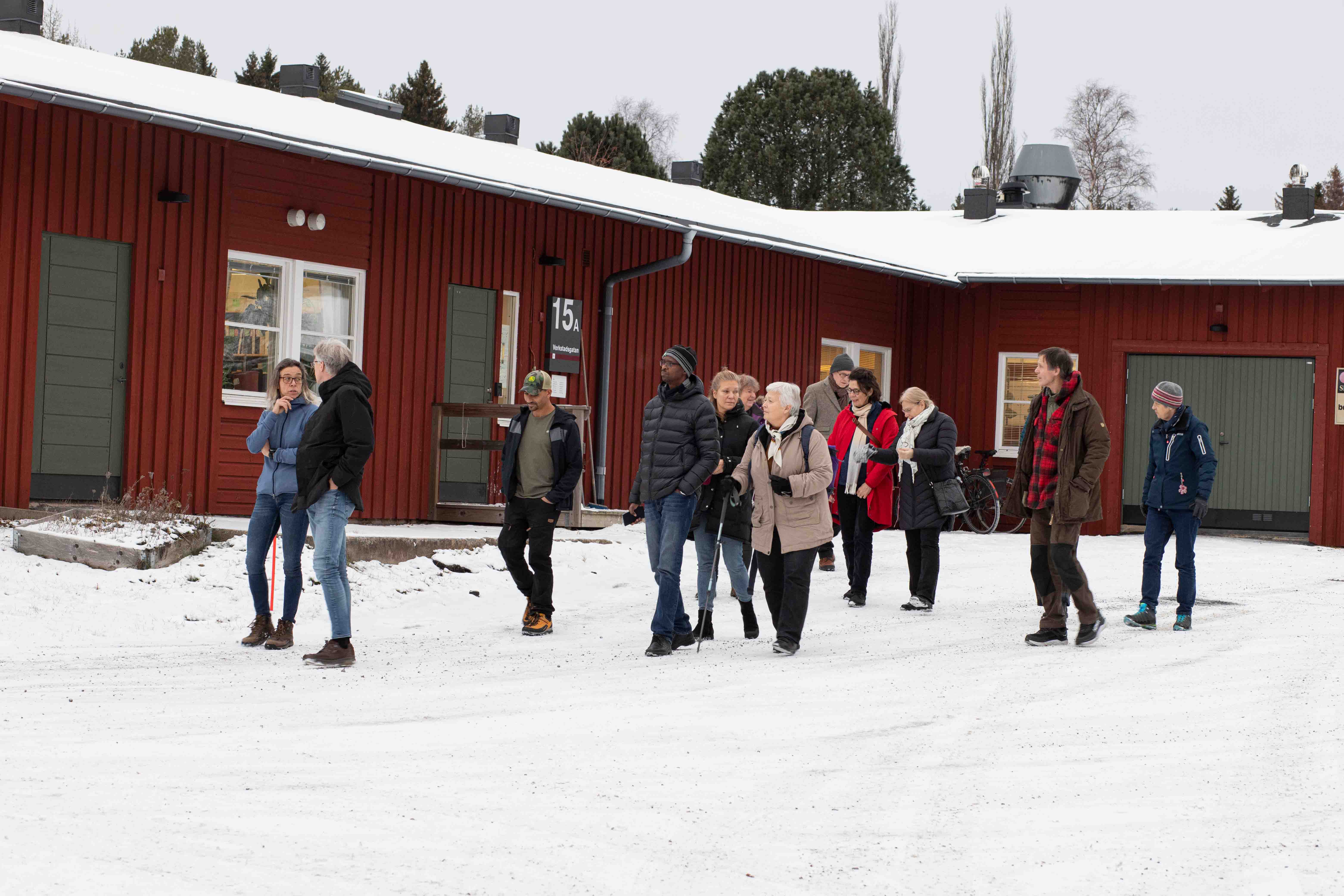 En grupp personer går i snön framför ett hus.