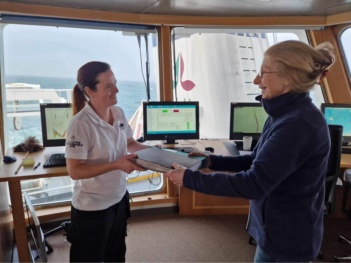A person hands over a binder to another person on a ship.