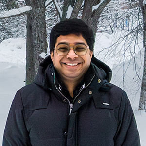Portait photo of Vinod Kumar standing with a black jacket in a snowy landscape in front of a few trees in the back