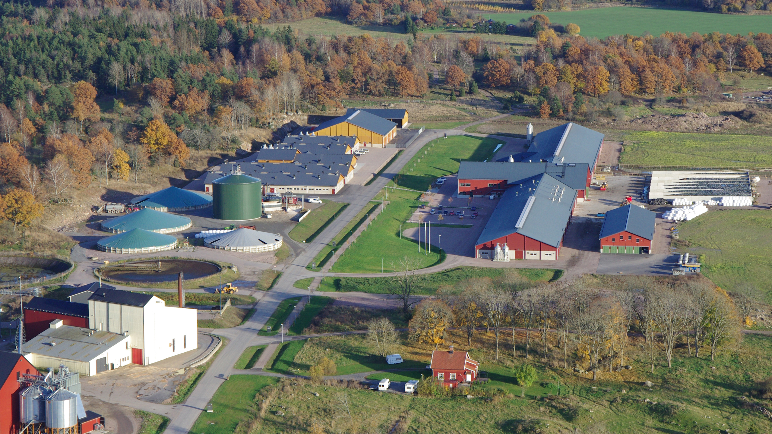 Flygbild över större lantbruksfastighet med olika byggnader, silos, biogasanläggning mm. omgivet av jordbruks- och betesmark.