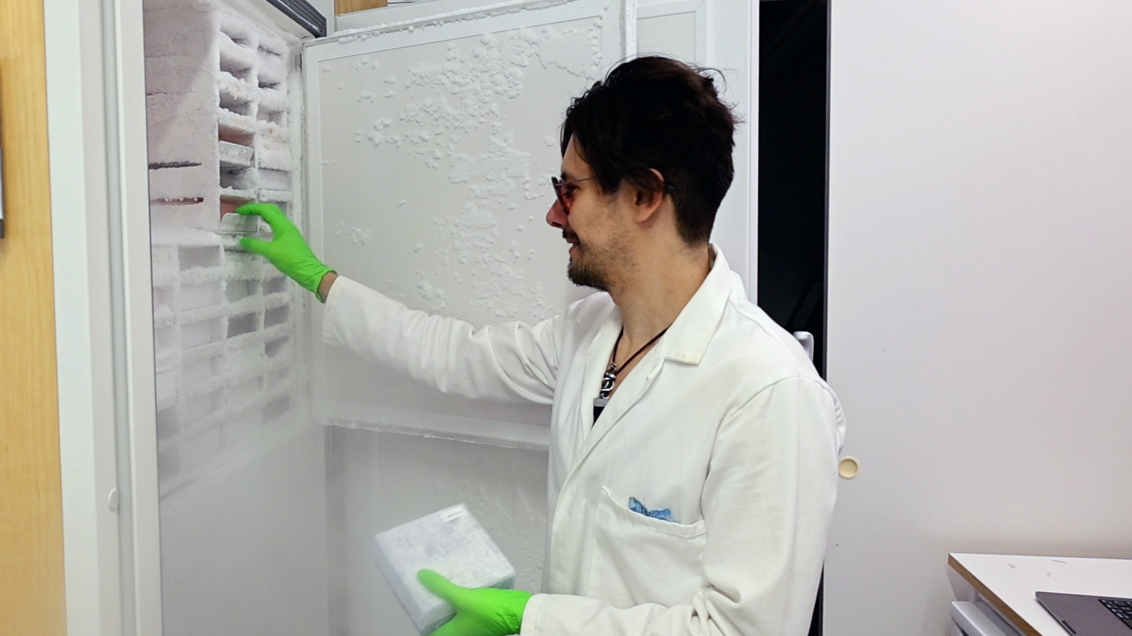 Lab worker standing by an open freezer with samples. Photo.