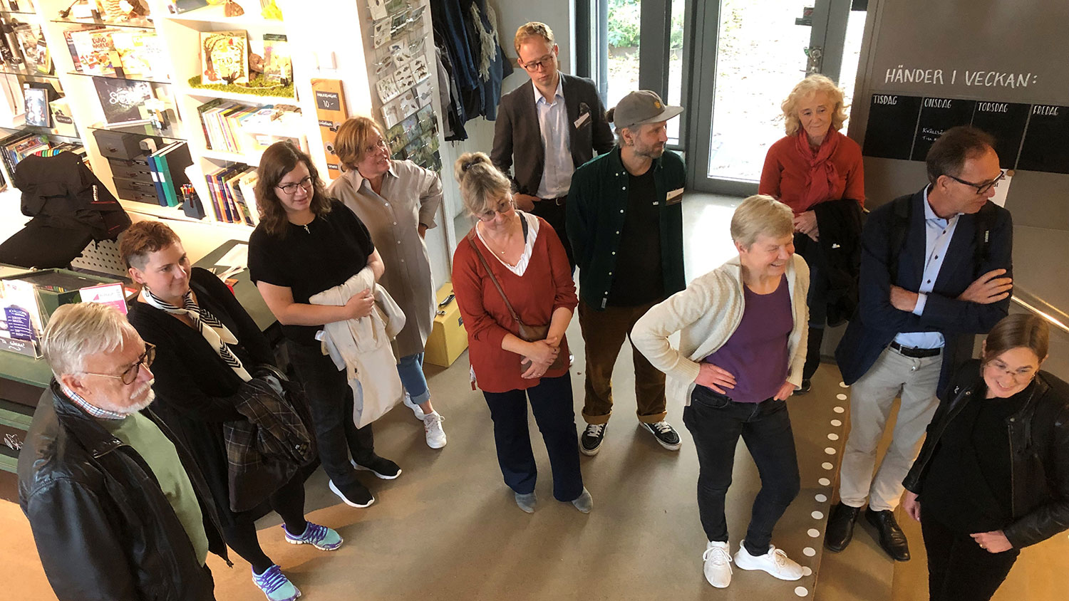 En grupp med elva personer som står på golvet inomhus, fotot taget snett uppifrån.