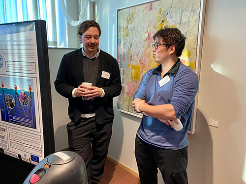 Two young men stand talking to each other, next to a scientific poster. Photo.