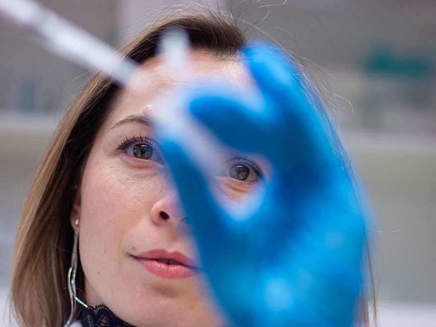 En närbild på en ung forskare som håller i ett provrör och en pipett, på handen har hon en blå handske. Foto.