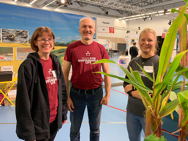 Tre personer står i en mässhall. Foto.