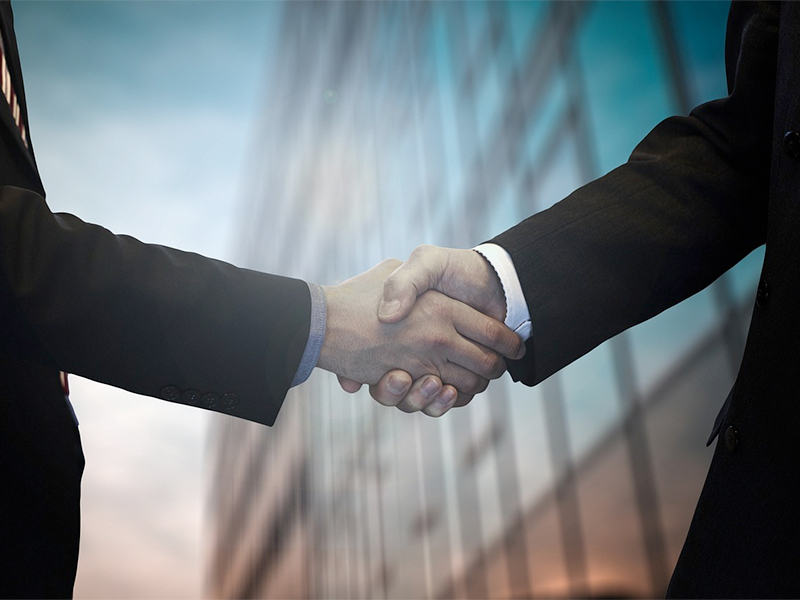 Two people shaking hands outside of a building. Photo.