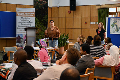 About 20 African women and men, sitting around round tables and discussing. Photo.