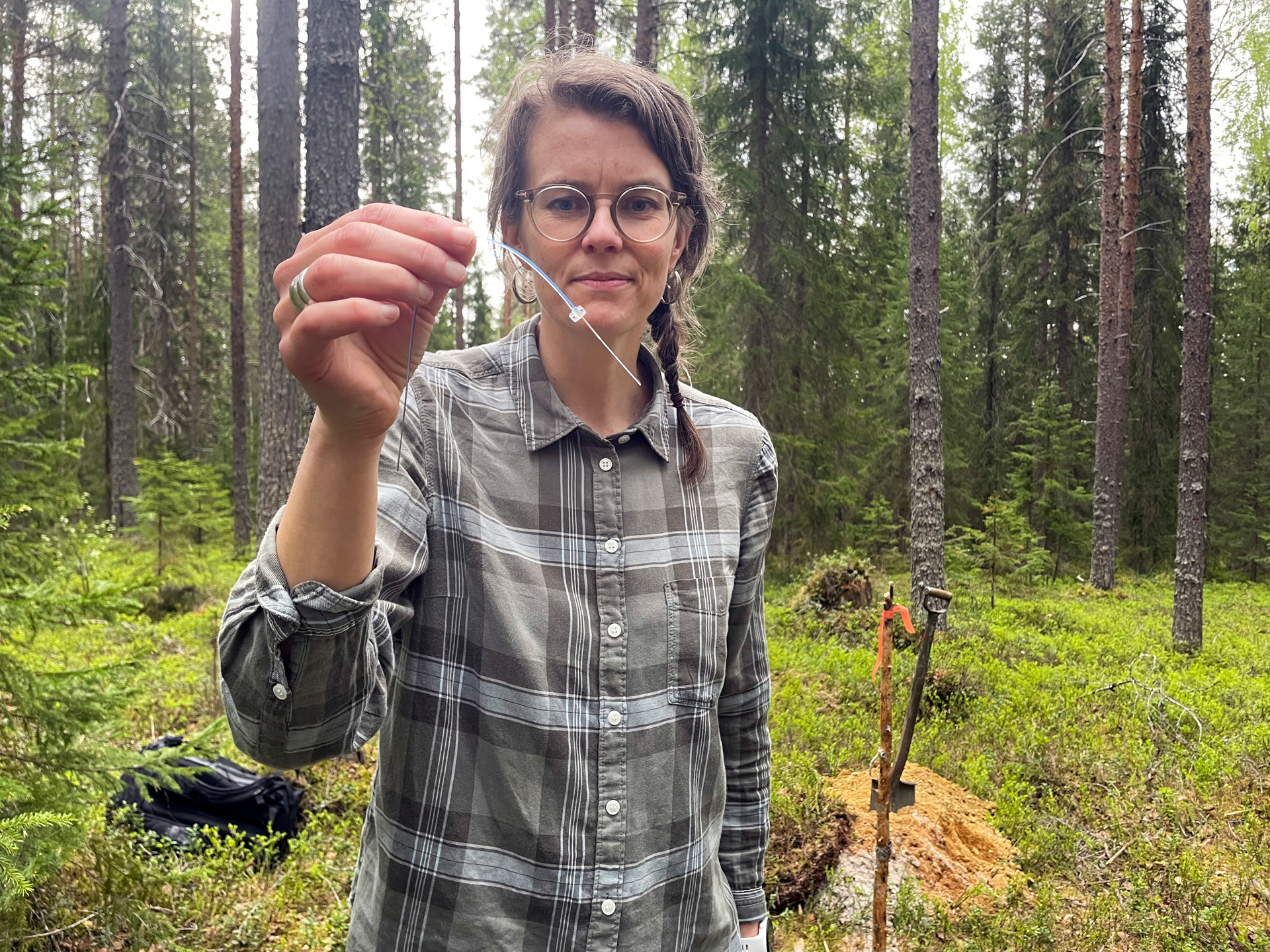 Sandra Jämtgård i skog, håller upp ett trådliknande föremål.