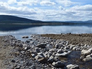 vatten rinner mellan sten och grus  med sjö och berg i bakgrunden