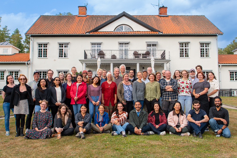 Ett gruppfoto framför en vit byggnad. Foto.