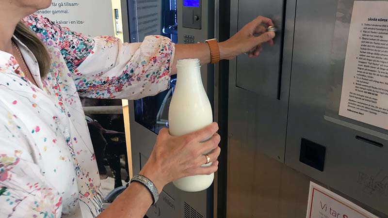 Close-up of a hand holding a bottle of milk at the milk dispenser. Photo.