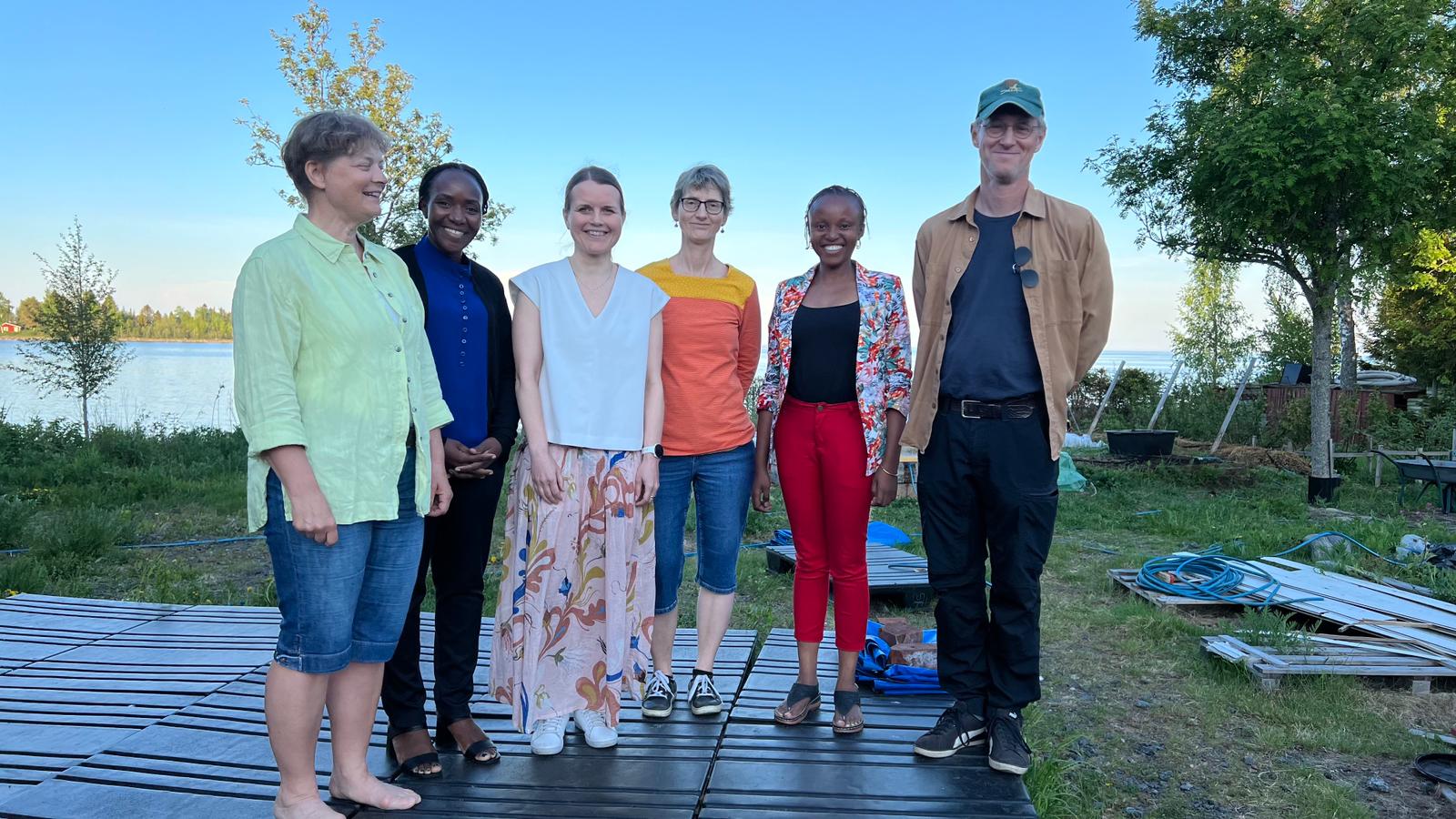 A row of six people standing in a row looking into the camera, smiling.