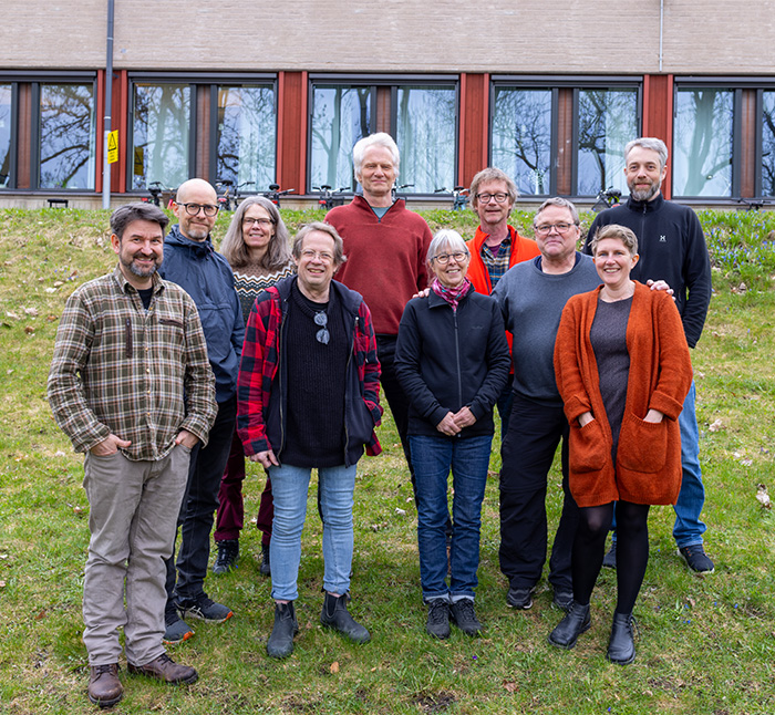 Grupp av människor står uppställda i gruppbild på gräsplätt framför kontorshus. Foto