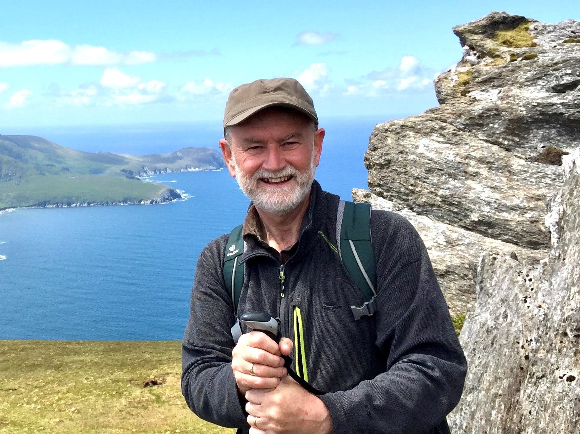 Man med vitt skägg och kikare står med ryggen mot havet Foto