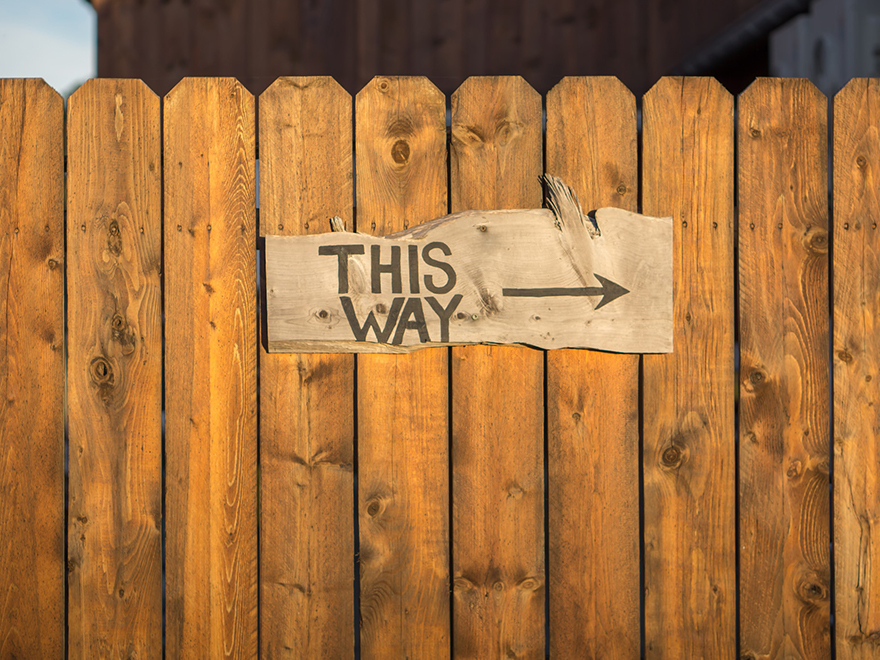 Foto av ett staket där det sitter en skylt som det står "this way" på med en pil till höger. 