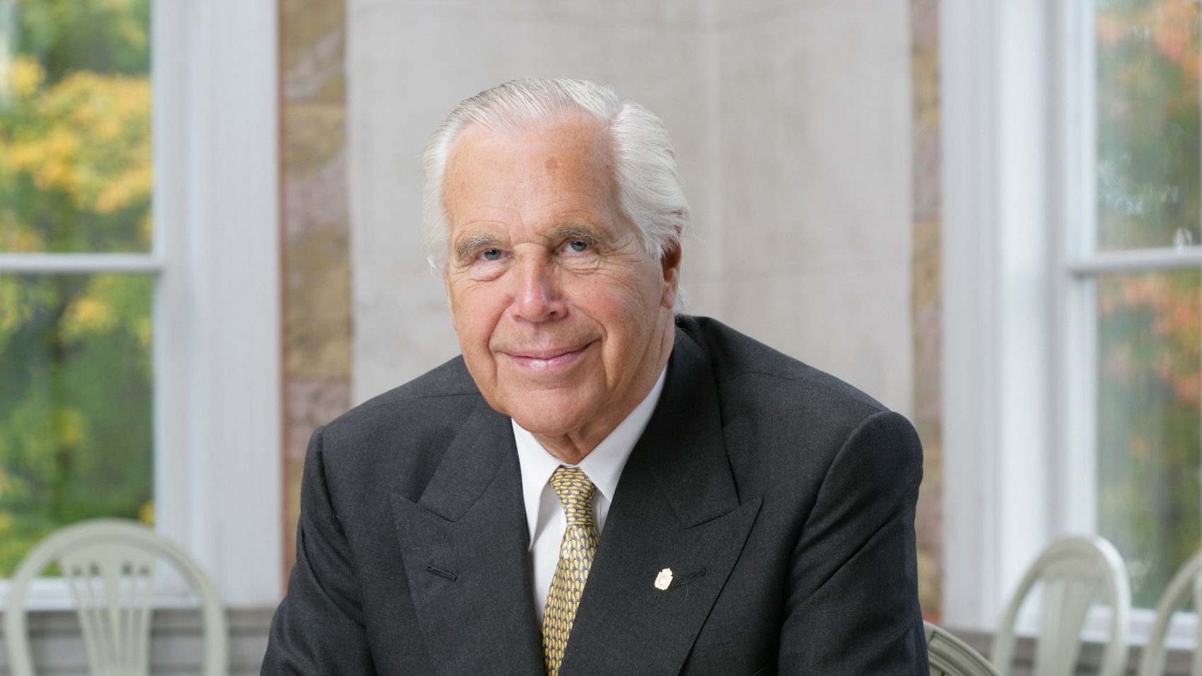 An elderly man in a suit and tie sitting at a table.
