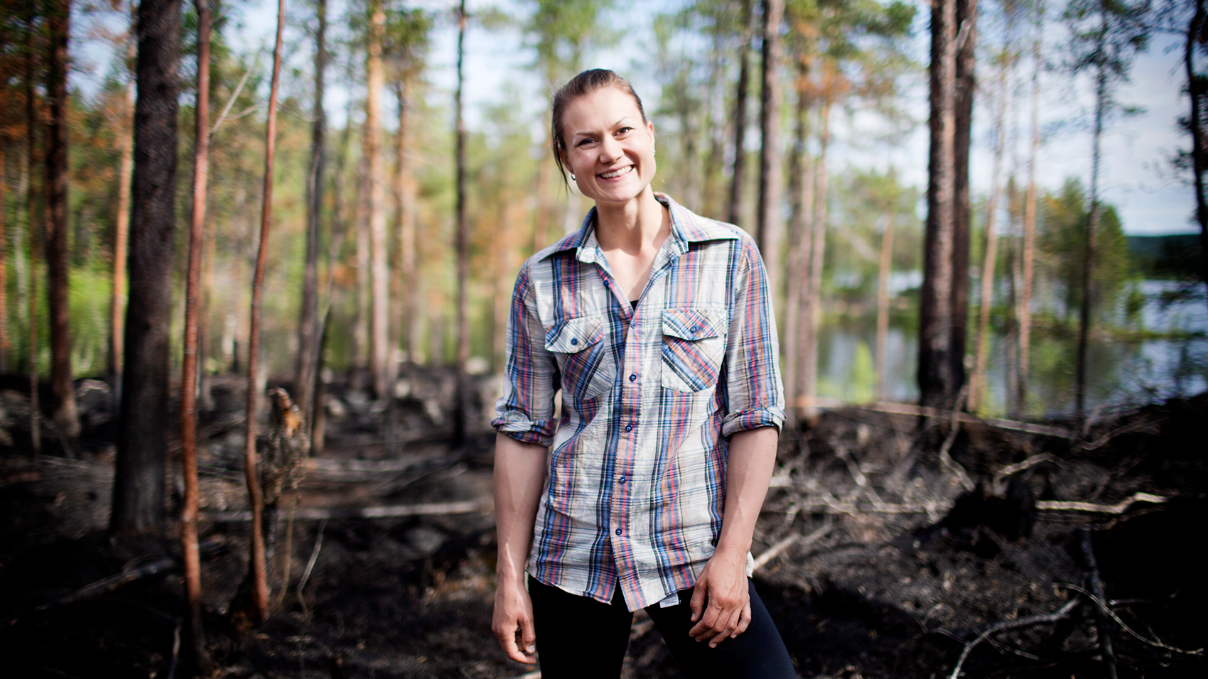 A woman standing in the woods with a smile on her face.