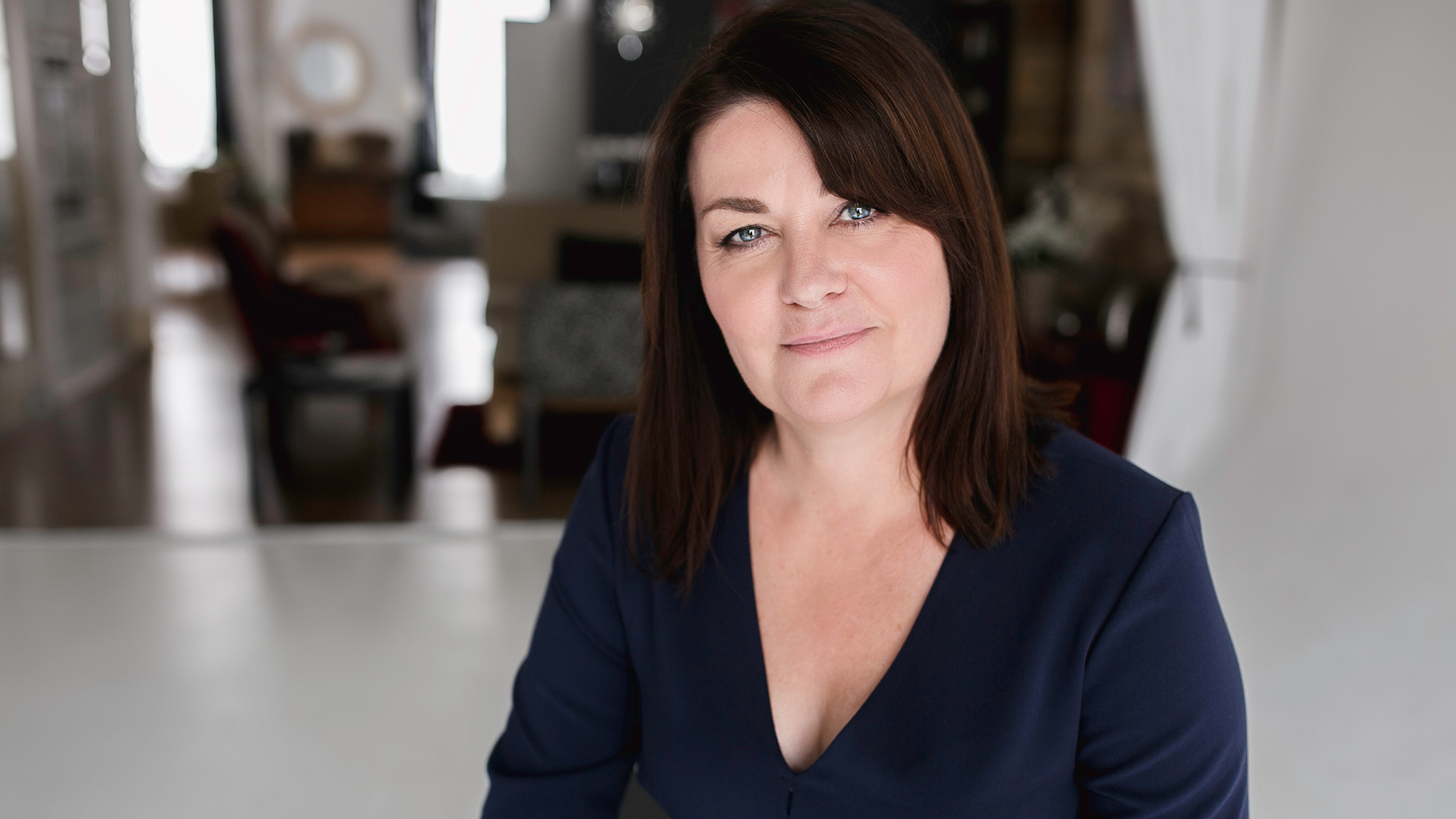 A woman with dark hair, wearing a dark blue shirt posing for an image.