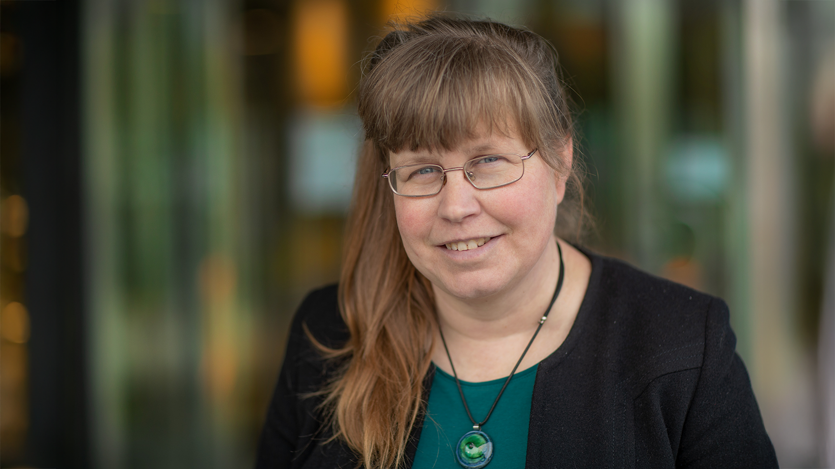 A woman with brown long hair and wearing glasses and a green shirt.