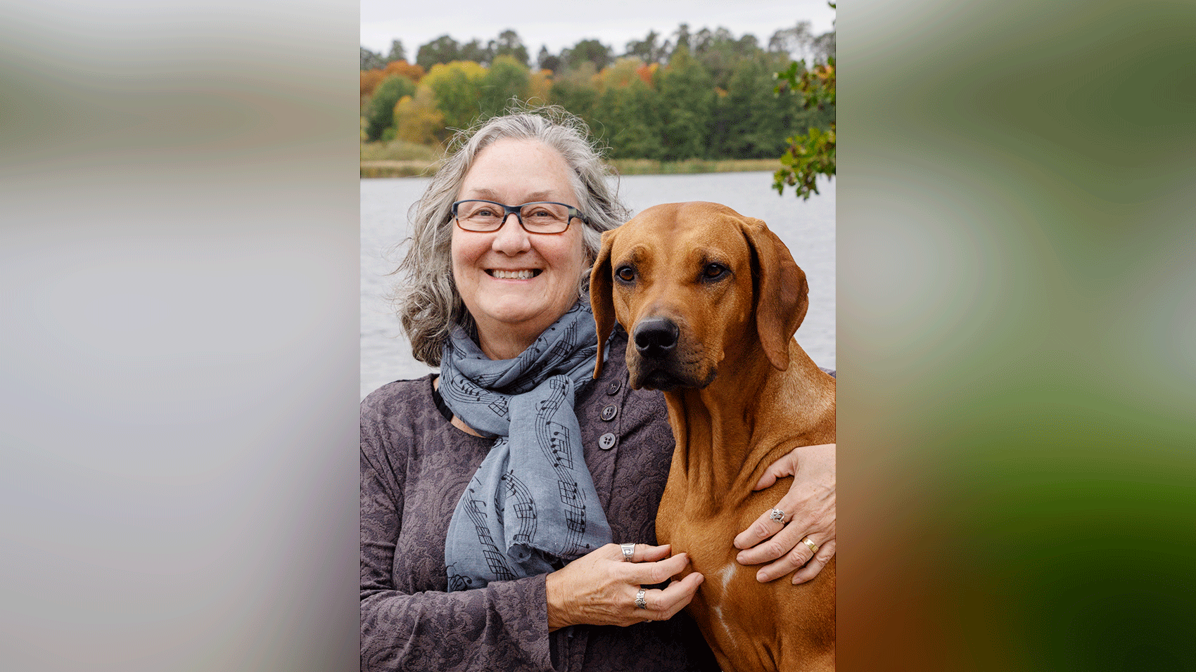 A woman holding a dog in front of a body of water.