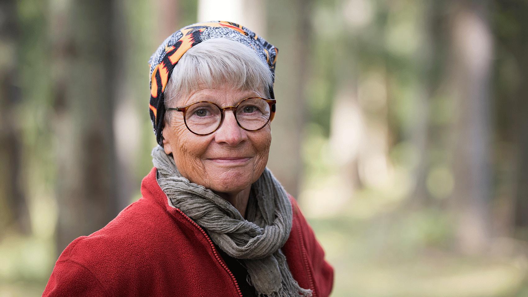 An elderly woman with a scarf, a red jacket and glasses.