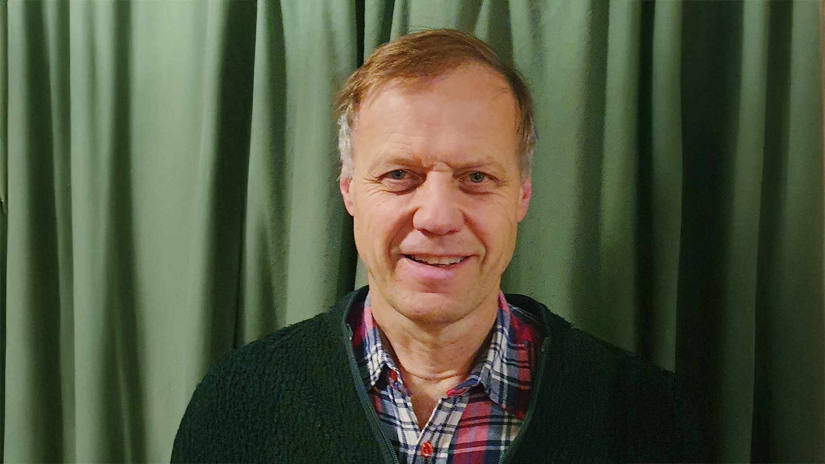 A man standing in front of a green curtain.