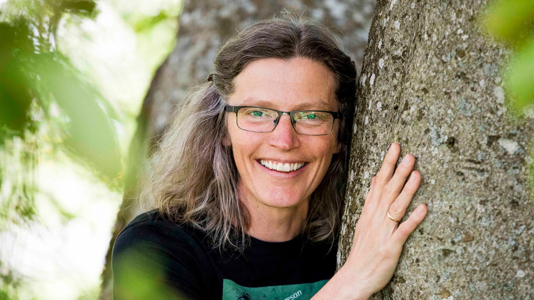 A woman wearing glasses hugging a tree.