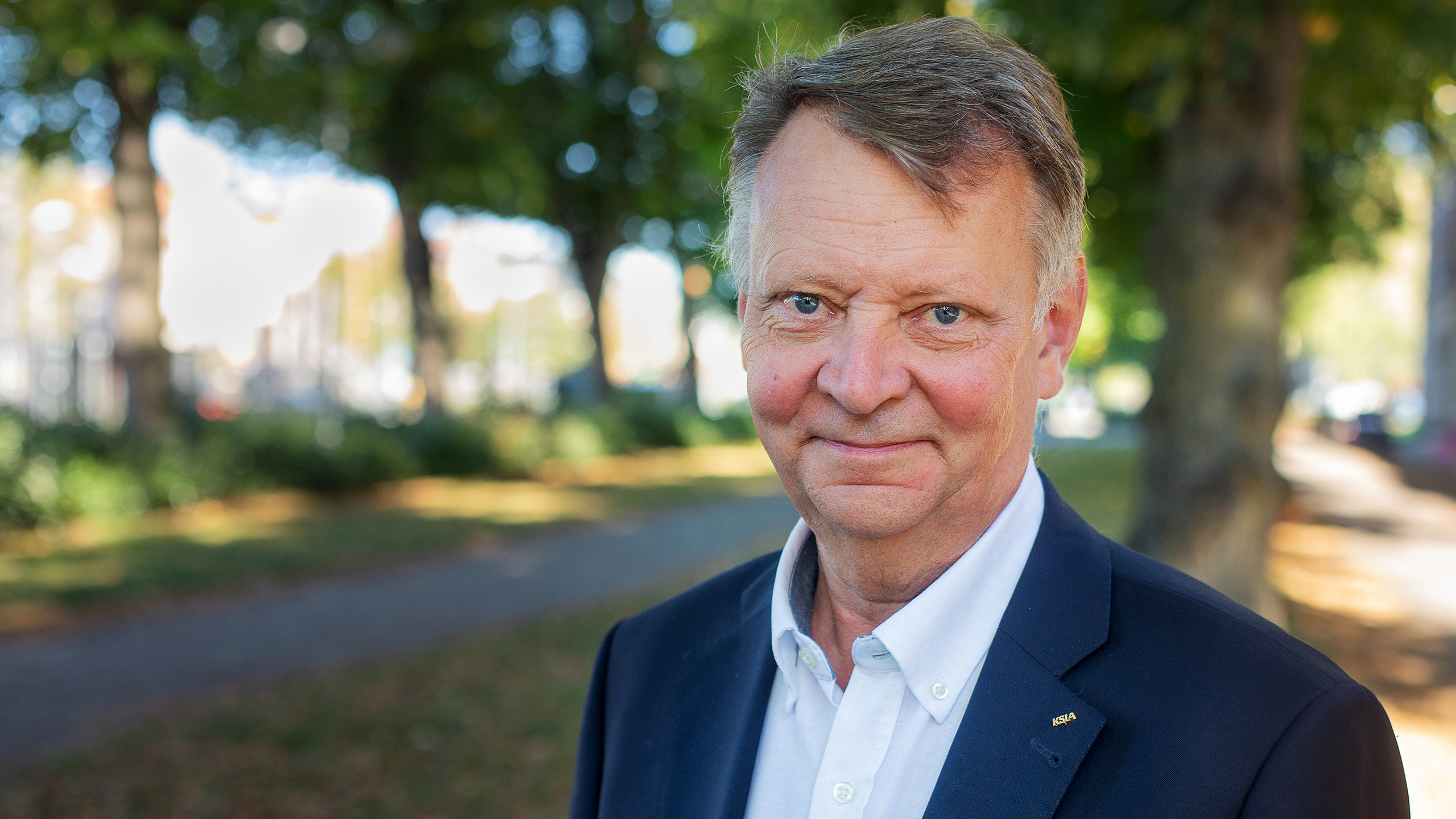 A man in a suit smiles into the cameran.
