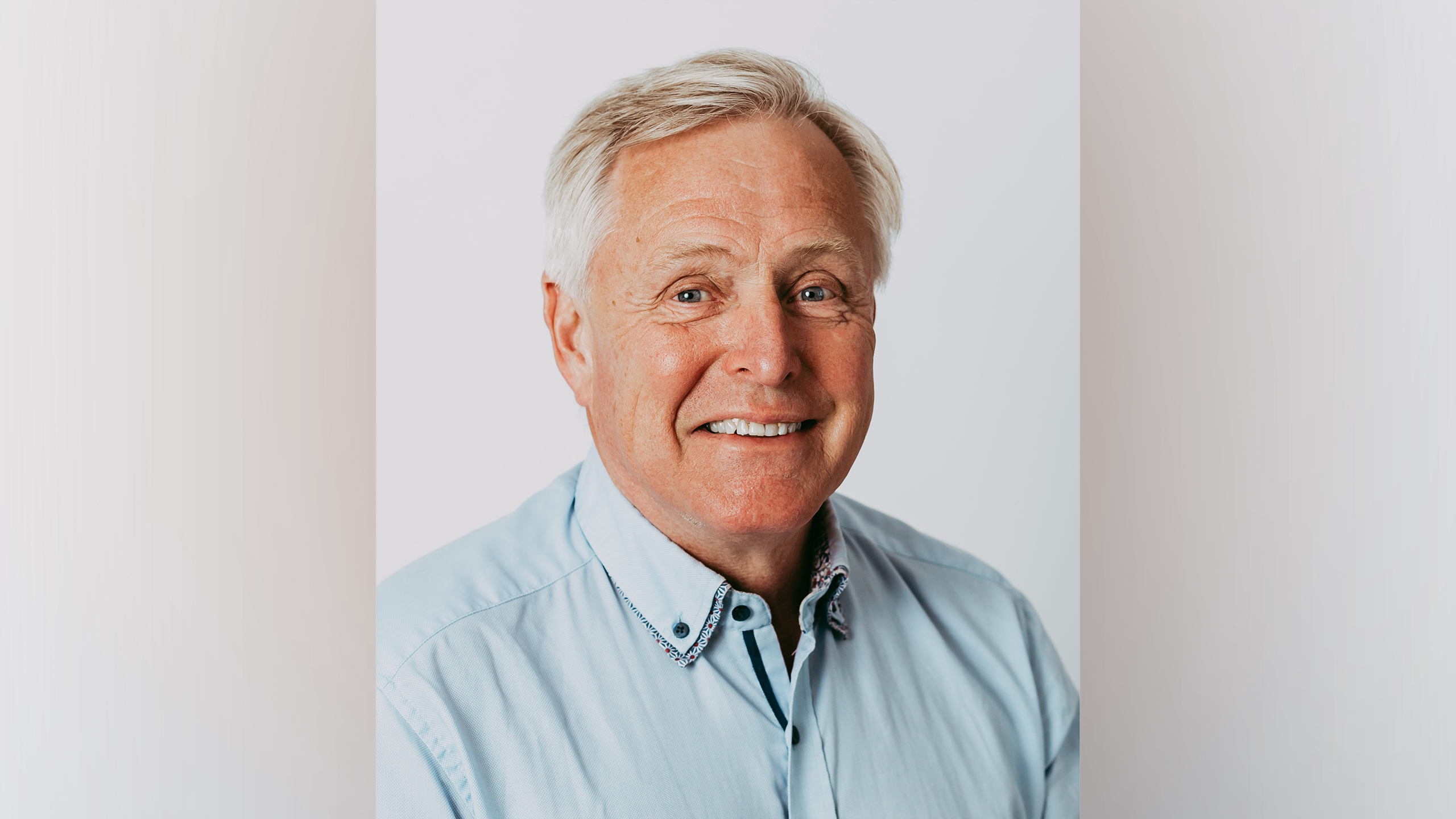 A smiling man with grey hair and a light blue shirt.