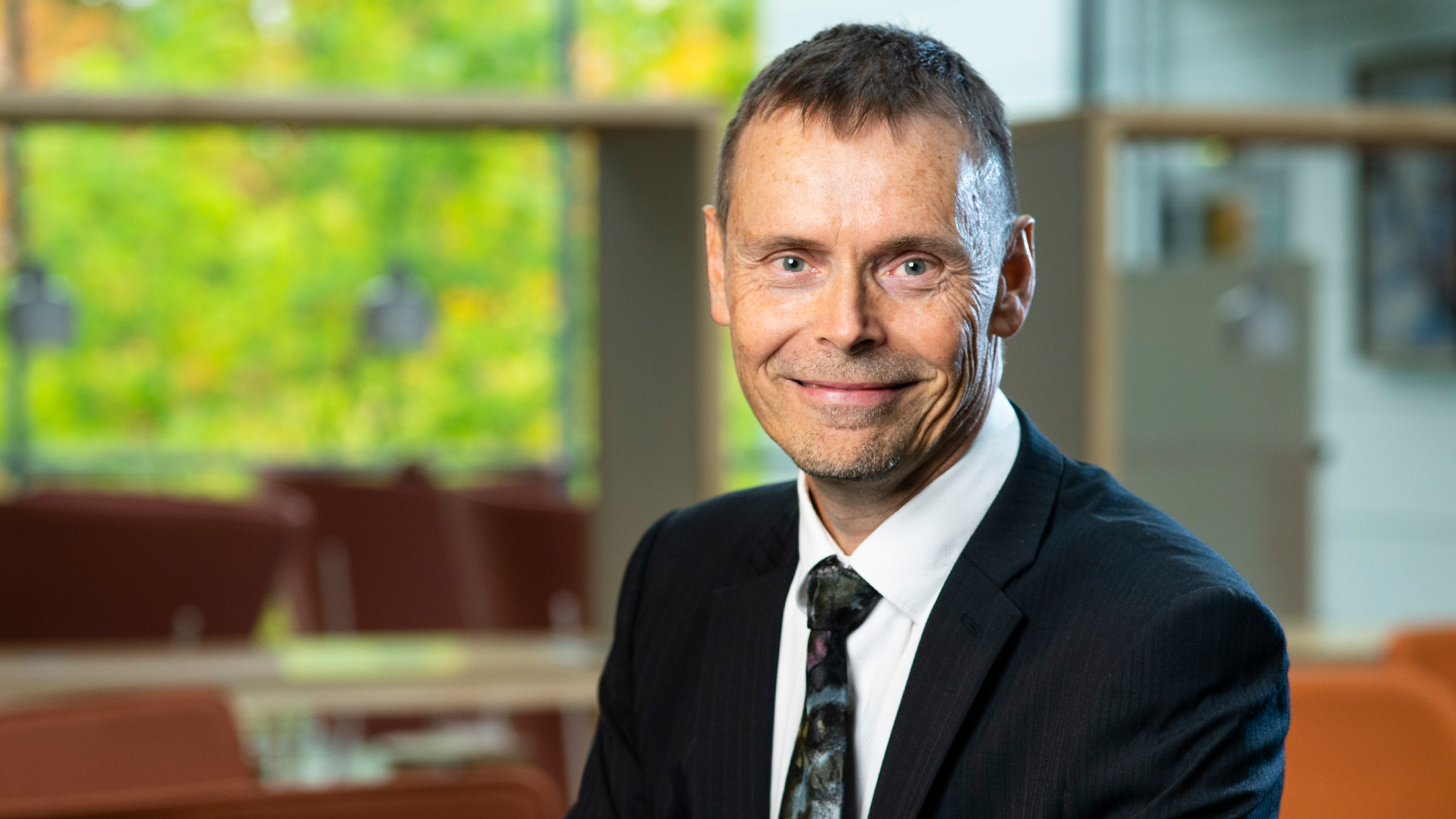 A smiling man in a dark suit looks into the camera.