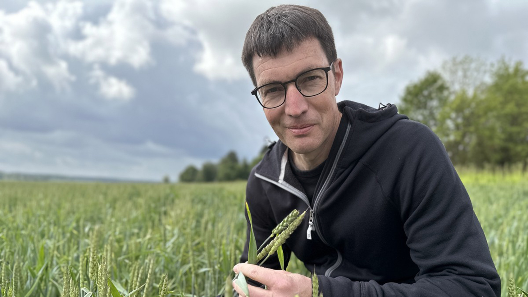 A man with dark hair and glasses sitting on a field.